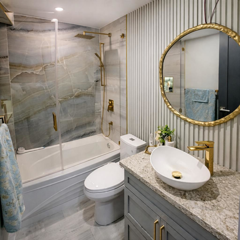 Modern bathroom with tub shower, marble tile walls, gold fixtures and round mirror vanity.
