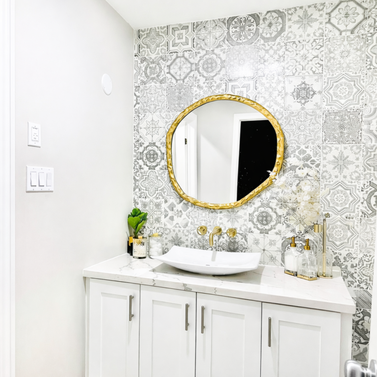 Modern bathroom vanity with patterned tile accent wall, gold mirror and vessel sink.