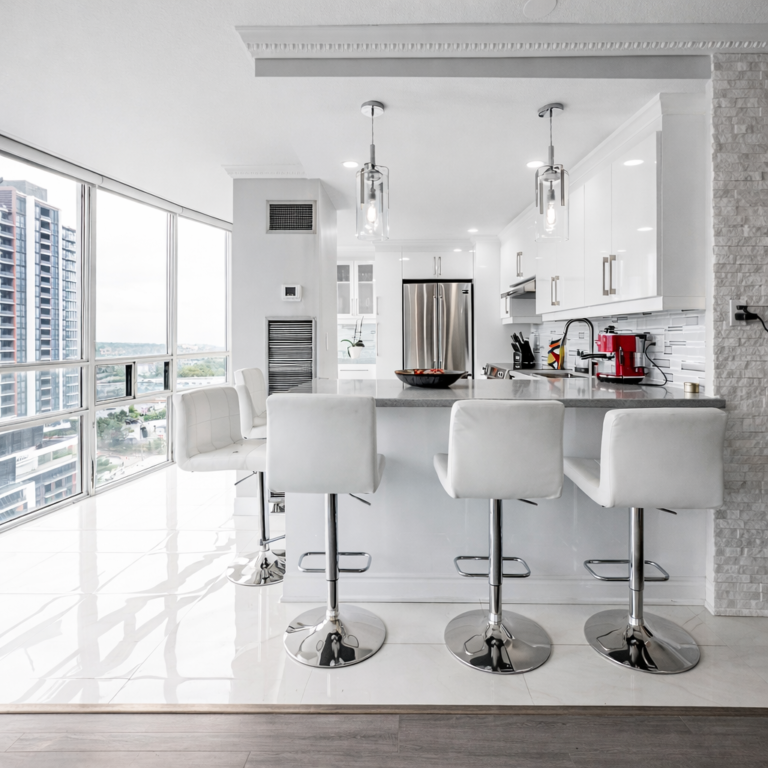 Modern condo kitchen renovation with white cabinets, gray countertop island, chrome bar stools, and floor-to-ceiling windows with city view.