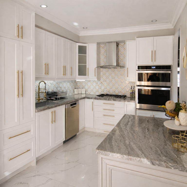 Modern white kitchen renovation with gold cabinet handles, patterned backsplash, and gray stone countertop.