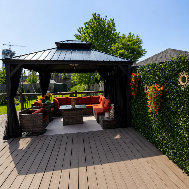 Modern backyard gazebo with a composite deck, comfortable outdoor seating, privacy wall, and landscaped outdoor living space.